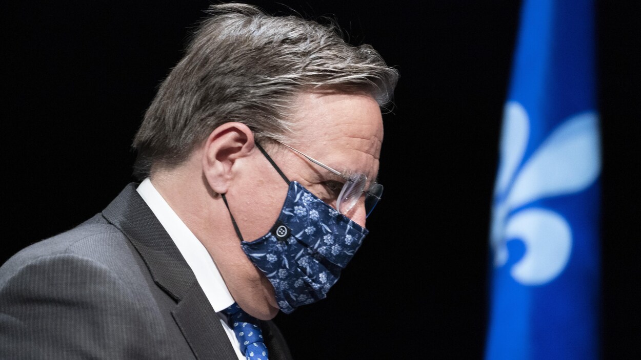 François Legault, portant un masque réutilisable, regarde vers le sol.