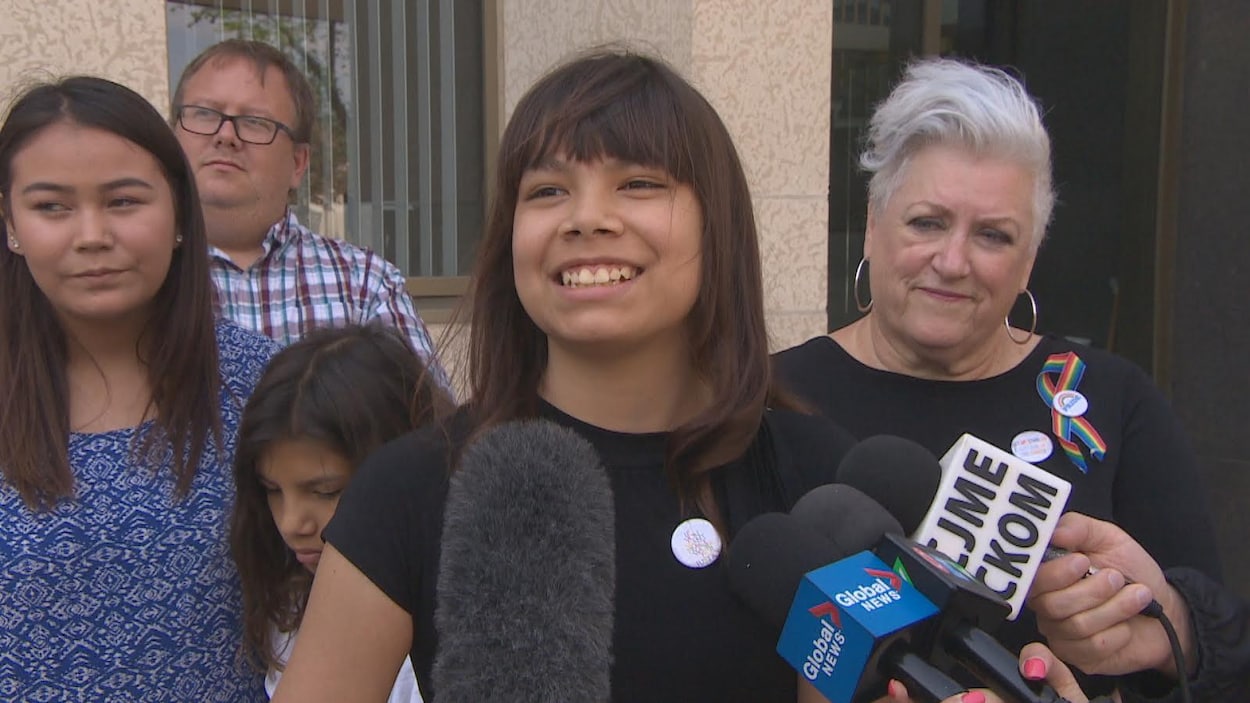 La femme entourée de trois de ses enfants, elle porte un ruban aux couleurs du drapeau LBGTQ.
