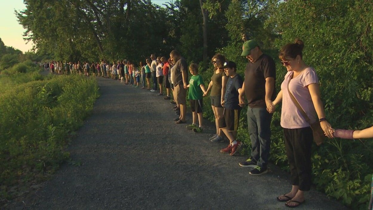 Plusieurs personnes forment une ligne sur un sentier en se tenant la main.