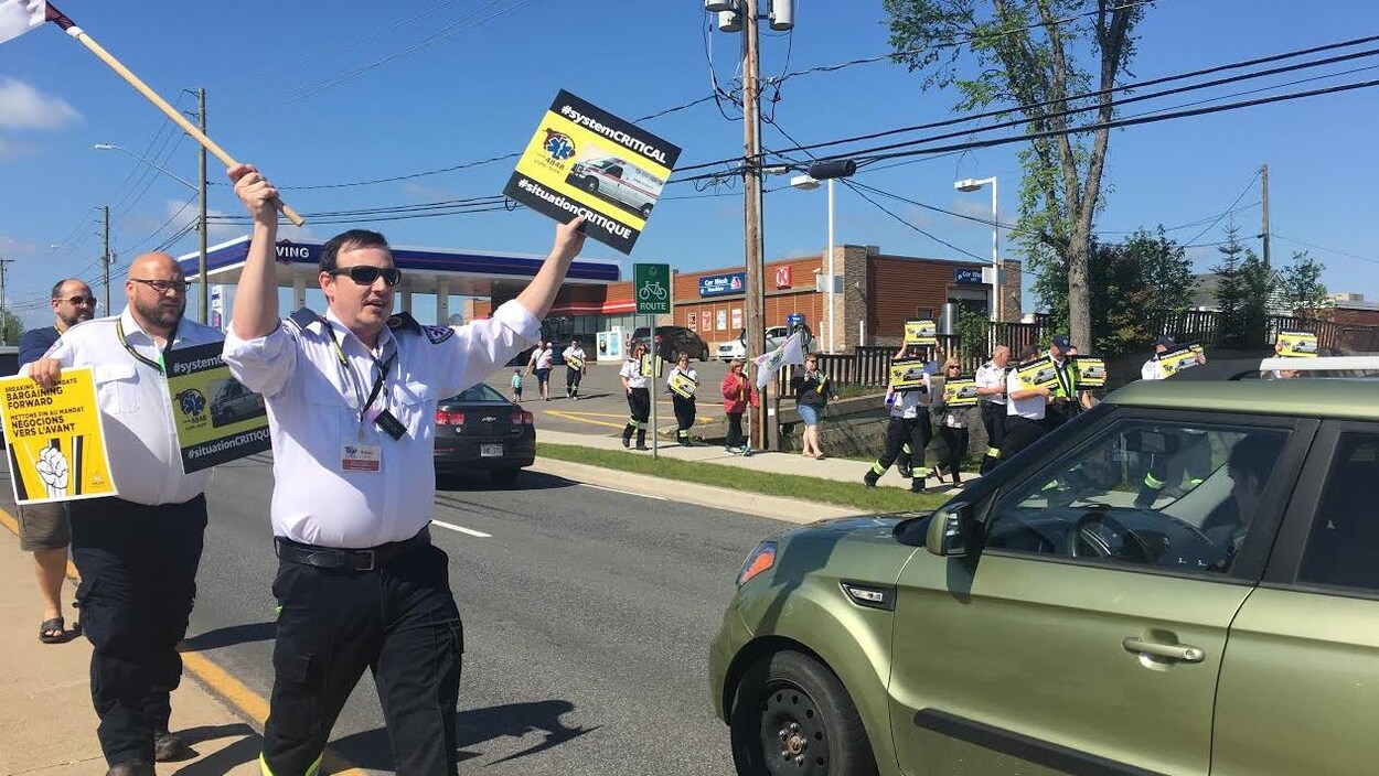 Des ambulanciers marchent le long d'une rue en brandissant des pancartes.