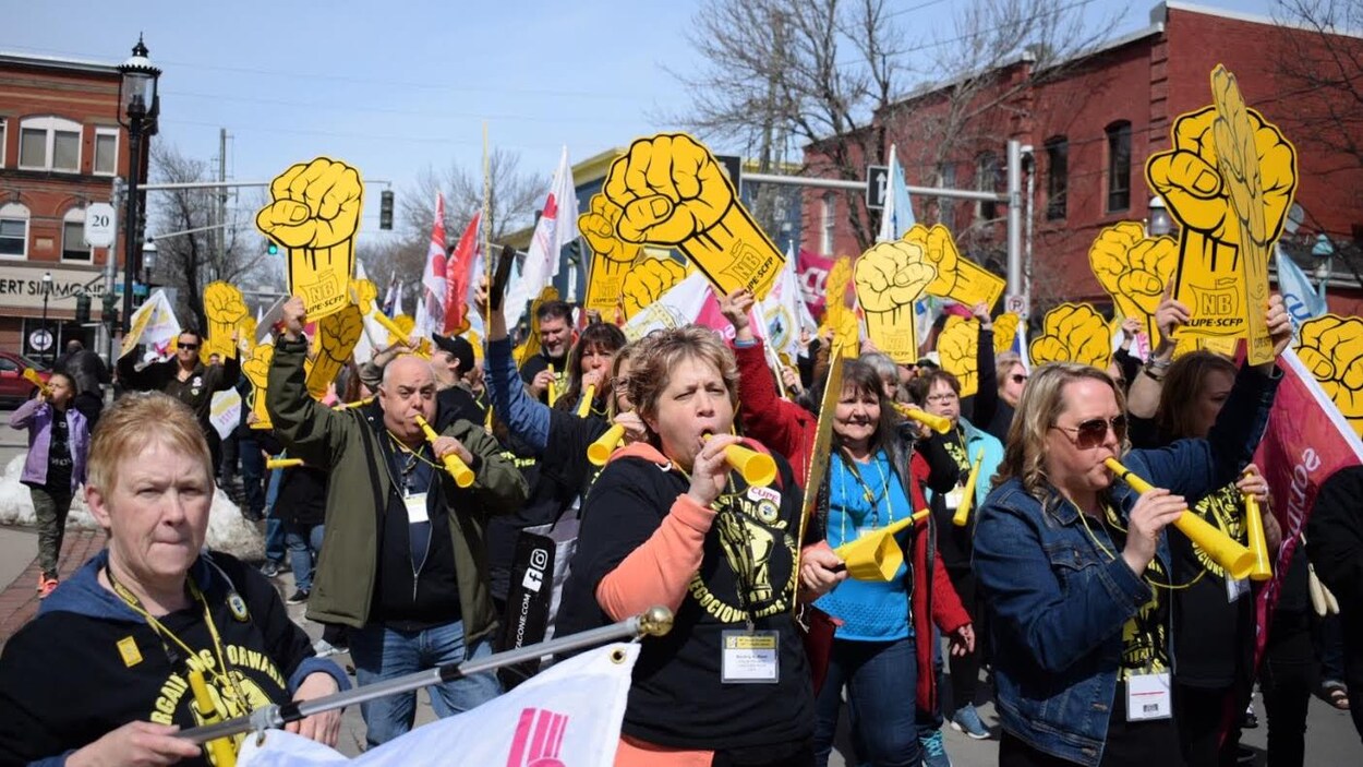 Des dizaines de personnes marchent en brandissant des pancartes syndicales et en soufflant dans des cornets.