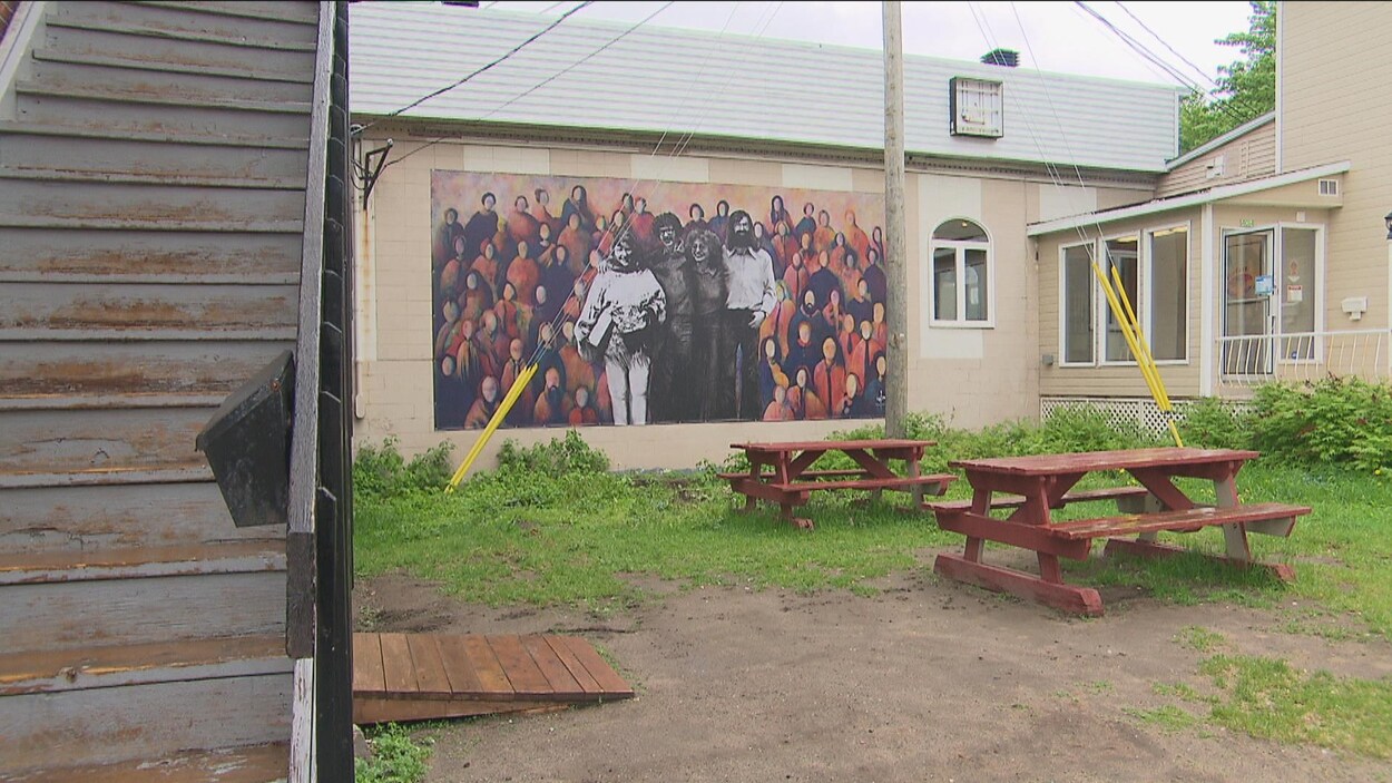 Une fresque représentant un groupe de personnes apparaît sur le mur d'un bâtiment beige.