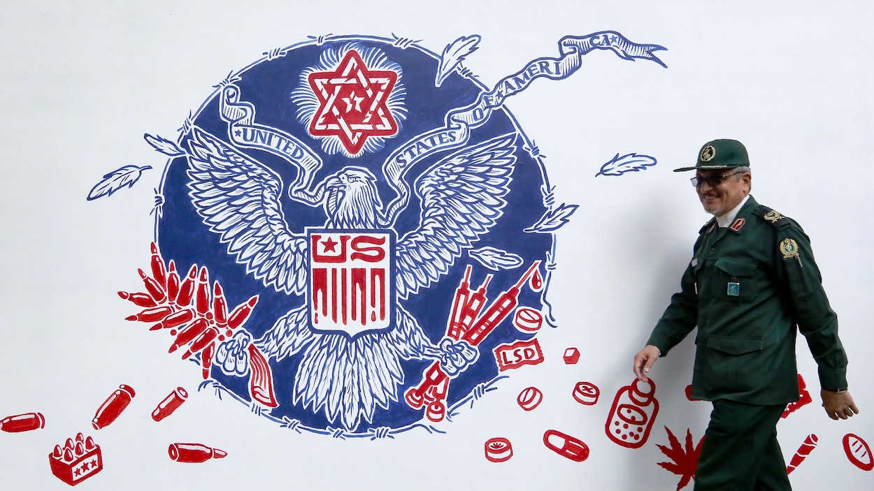 Un membre des Gardiens de la Révolution iraniens marche à côté d'une peinture représentant un aigle, symbole américain, entouré de seringues, de drogues et de cartouches.