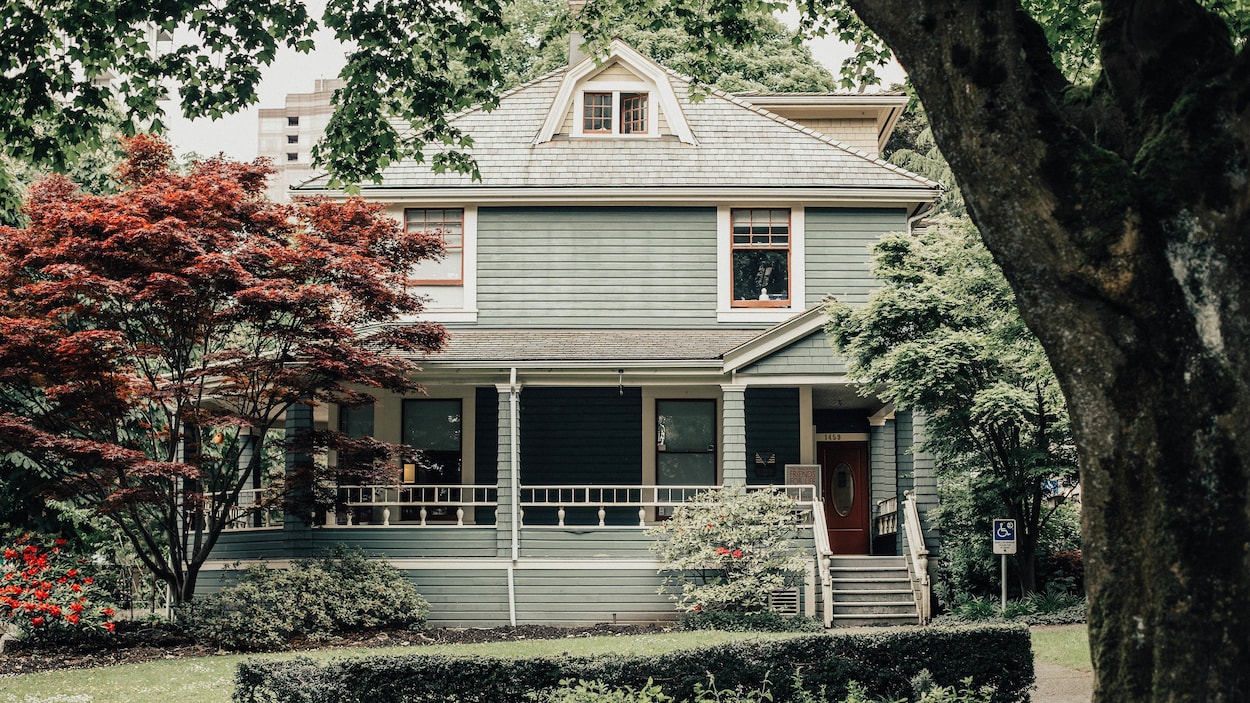Façade d'une maison sur deux étages entourée d'arbres.
