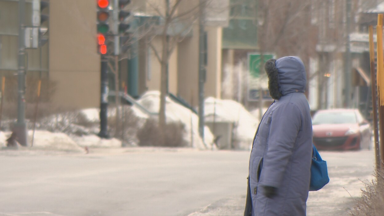 Une dame attend sur le trottoir vêtue d'un gros manteau d'hiver