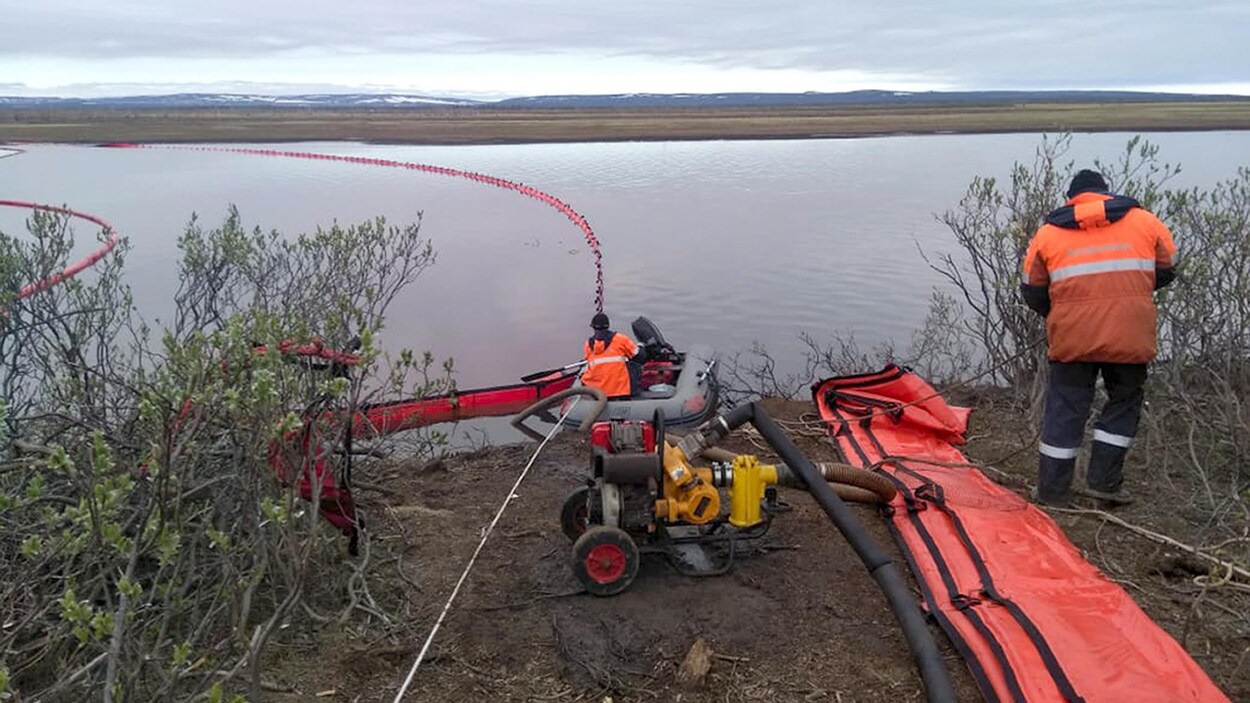 Des travailleurs s'affairent près de bouées destinées à contrôler les hydrocarbures dans l'eau.