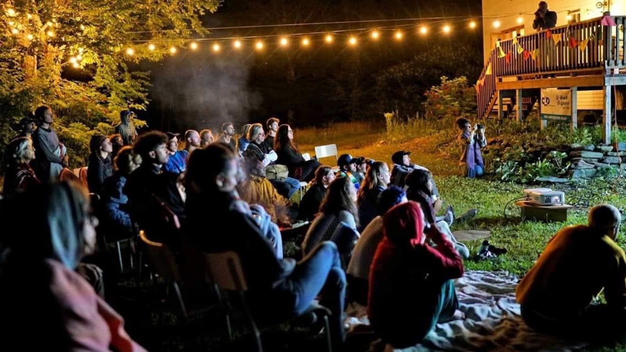 Des dizaines de personnes sont assises sur l'herbe dans la cour arrière du Salon58 pour assister à une projection d'un film de danse.