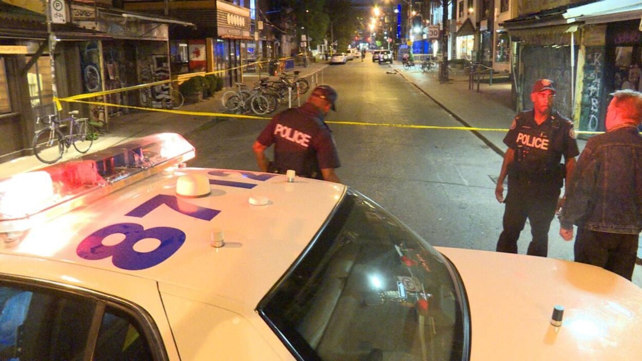 Photo d'une autopatrouille, d'une banderole jaune et de policiers bloquant une rue