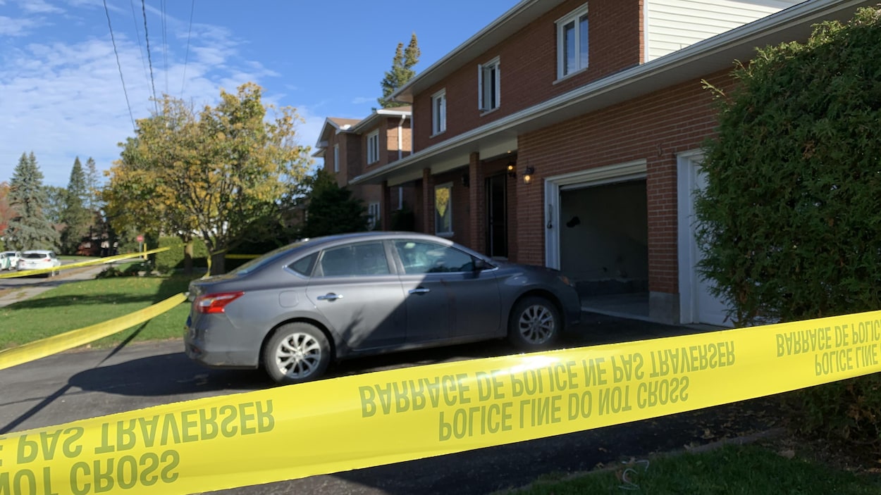 Une voiture stationnée devant une résidence de banlieue, à l'intérieur d'un périmètre policier.