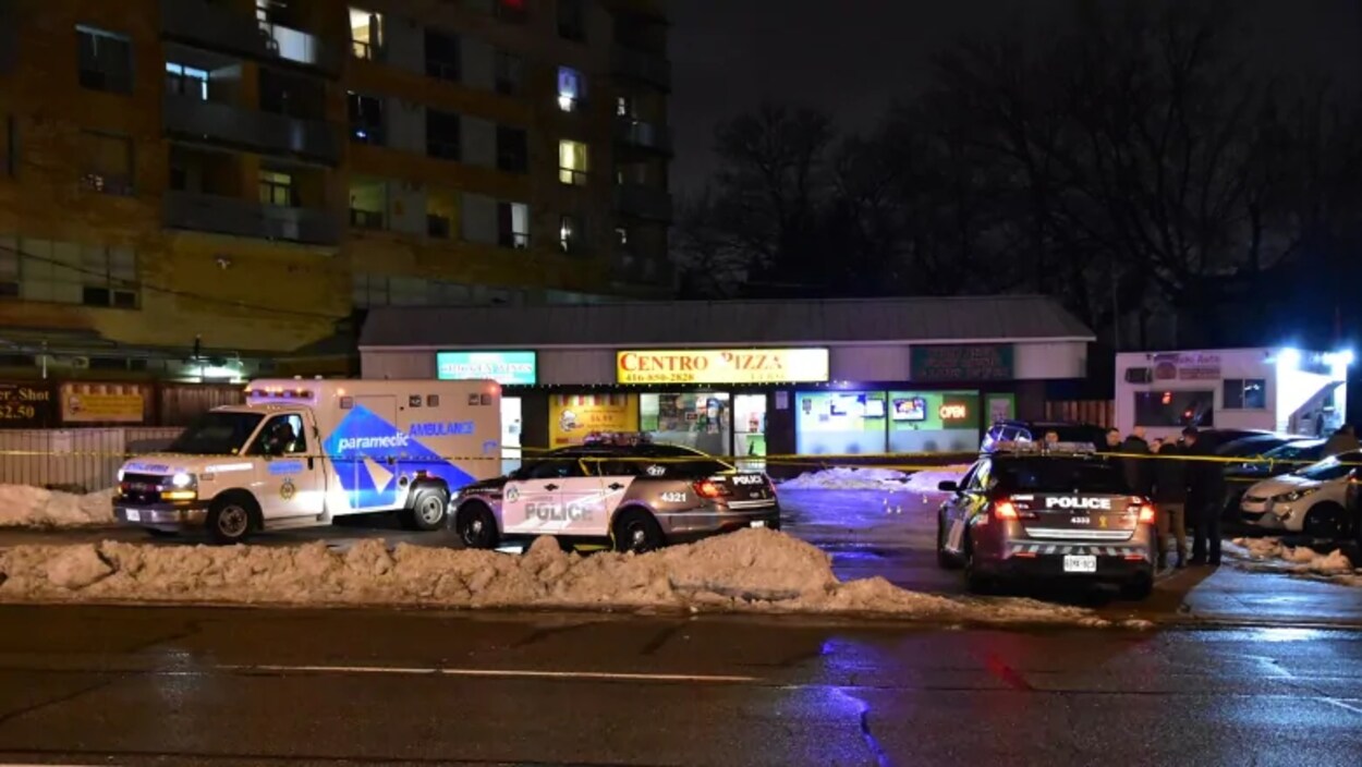 Des voitures de police et une voiture d'ambulanciers devant des commerces dans une rue la nuit.