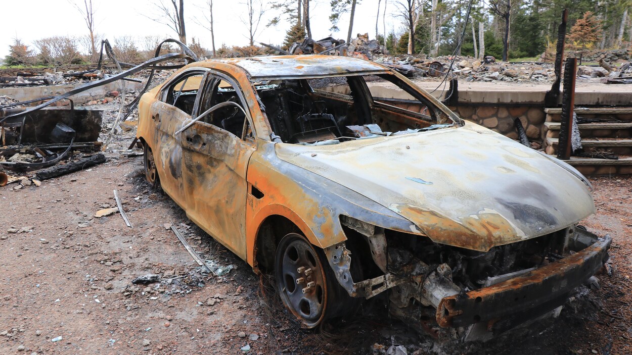 Voiture carbonisée parmi les ruines d'une maison.