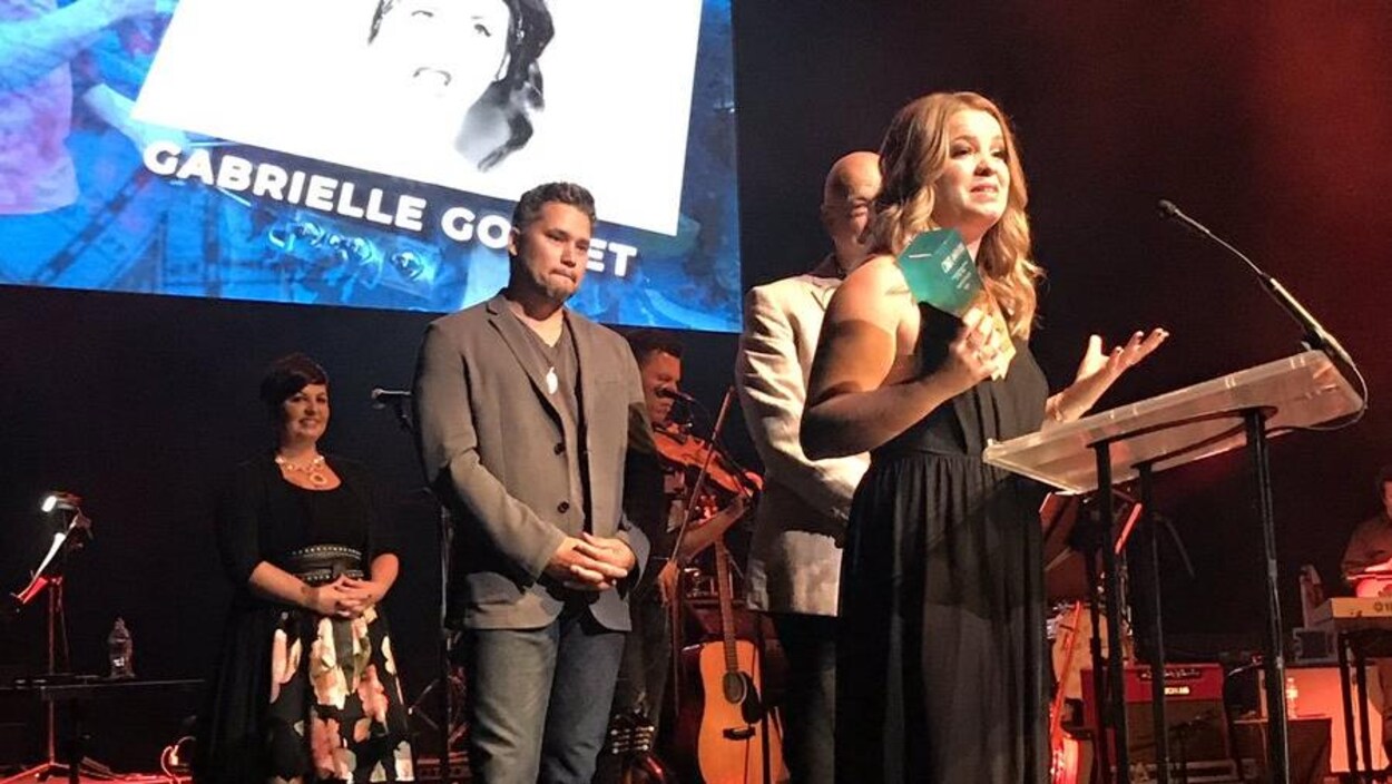 Une jeune femme en robe longue sur une scène lors d'un gala, trophée à la main
