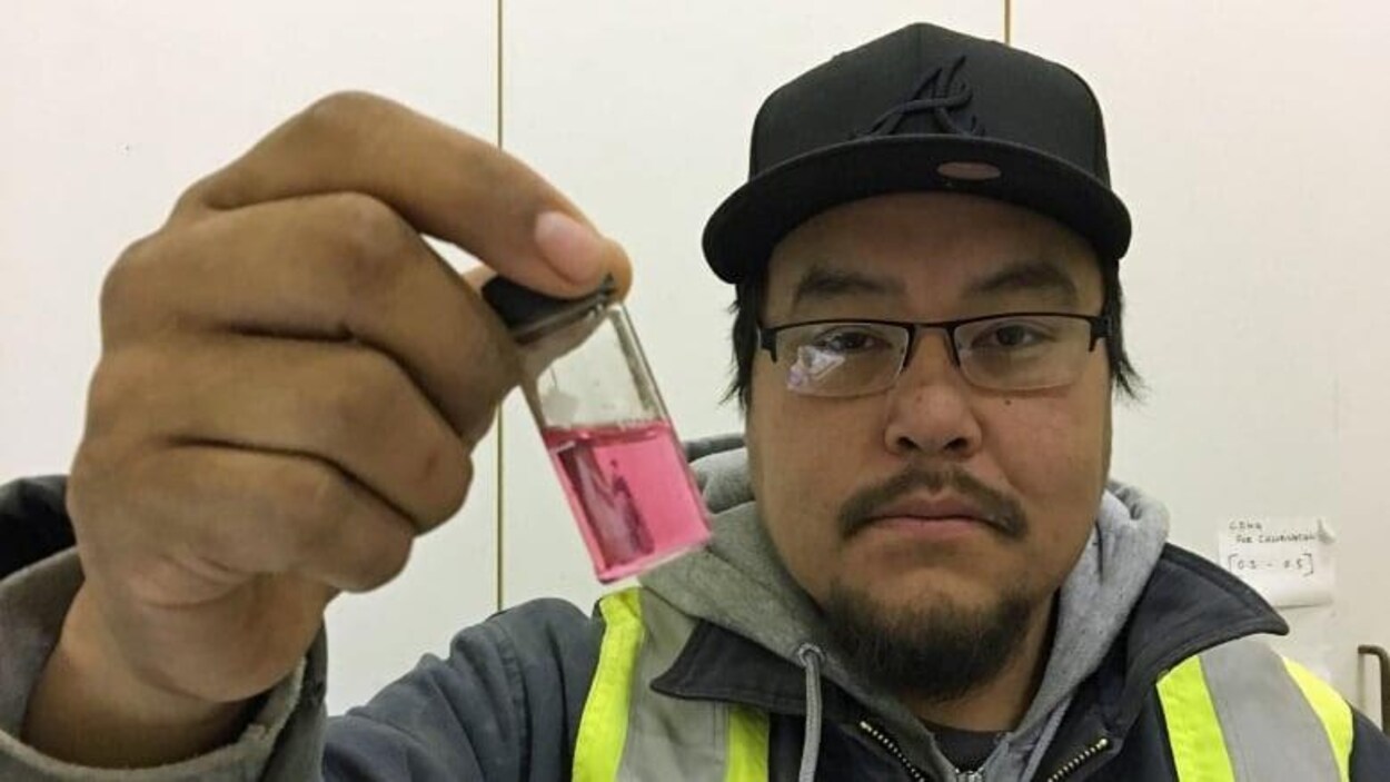 Un homme montre un échantillon d'eau rose dans une petite bouteille.