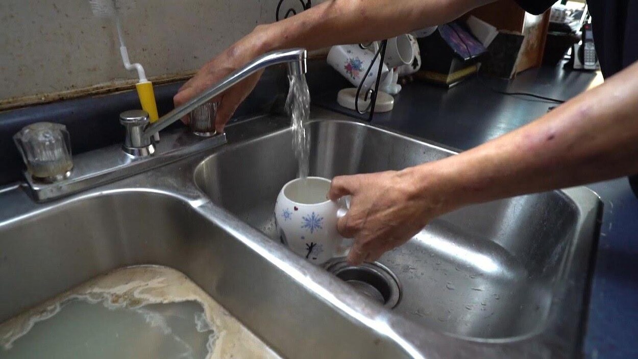 Une main actionne un robinet pour faire couler l'eau dans une tasse.