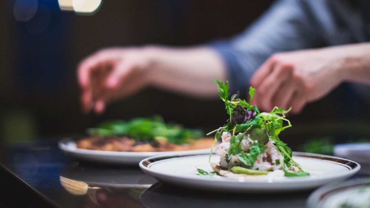 Plan serré de mains qui s'apprêtent à prendre une assiette de nourriture bien montée sur un comptoir de restaurant.