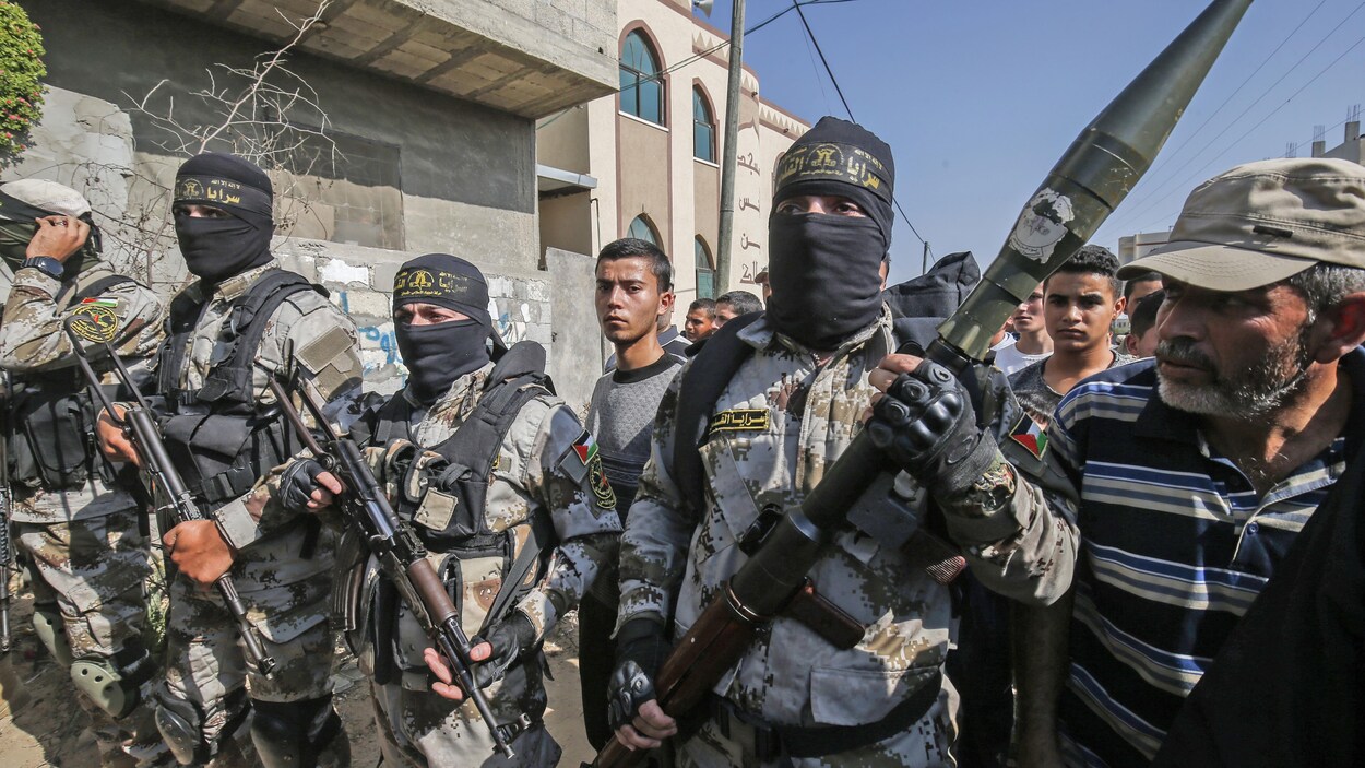 Des hommes masqués et en treillis militaire tiennent des armes dans leurs mains au milieu d'une foule.