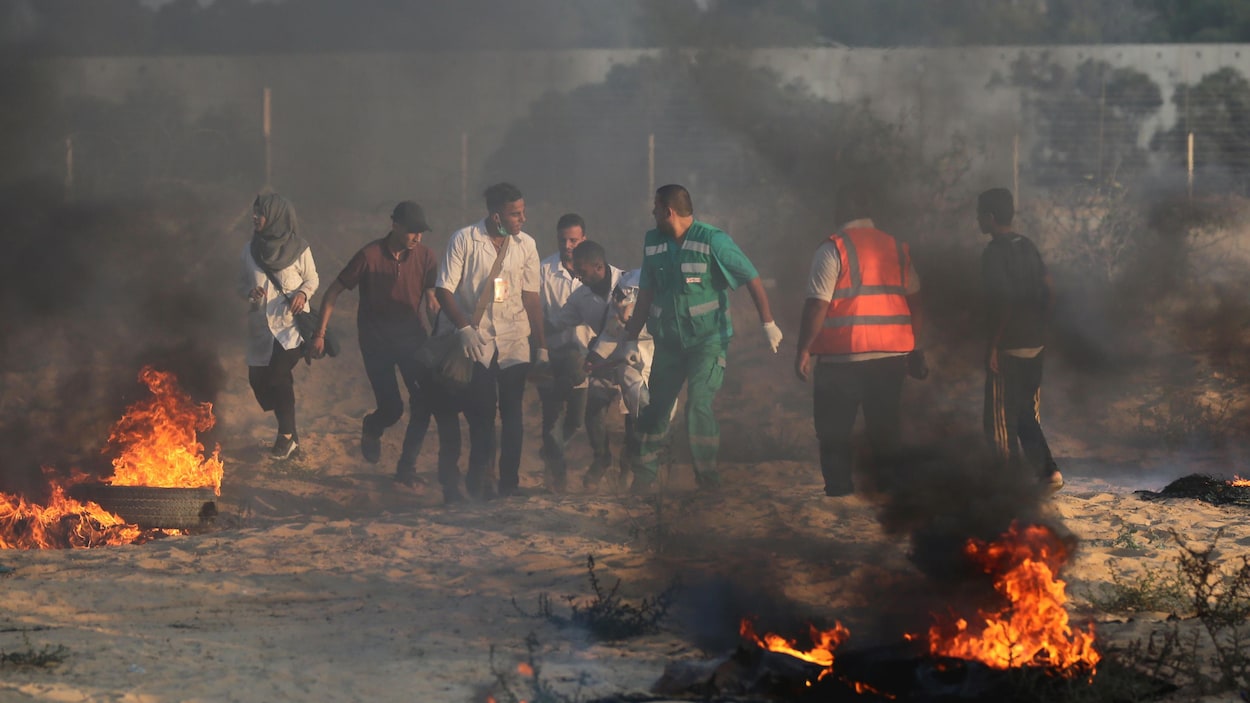 Des hommes et une femme transportent des blessés à travers de la fumée et des flammes à l'extérieur.