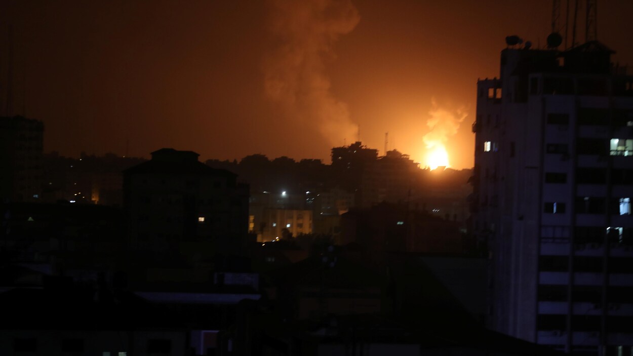 On voit des flammes derrière des immeubles d'habitation.