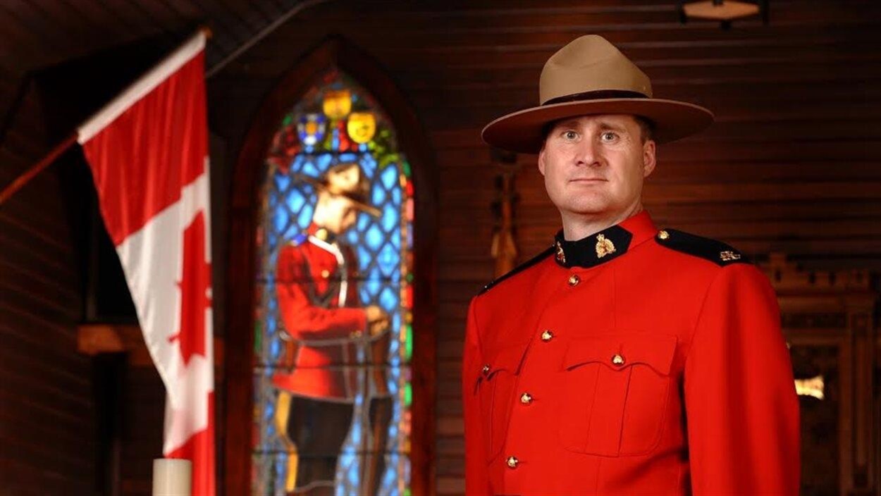David Wynn, vêtu d'un uniforme rouge de la GRC, près d'un drapeau canadien.