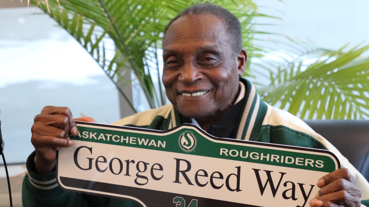George Reed tient une plaque de rue qui porte son nom.