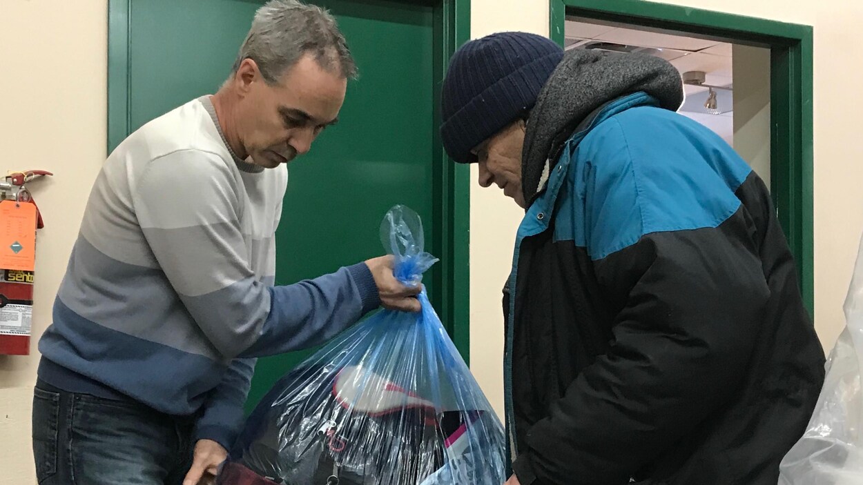Gilbert Vielfaure donne un sac de vêtements à un homme.