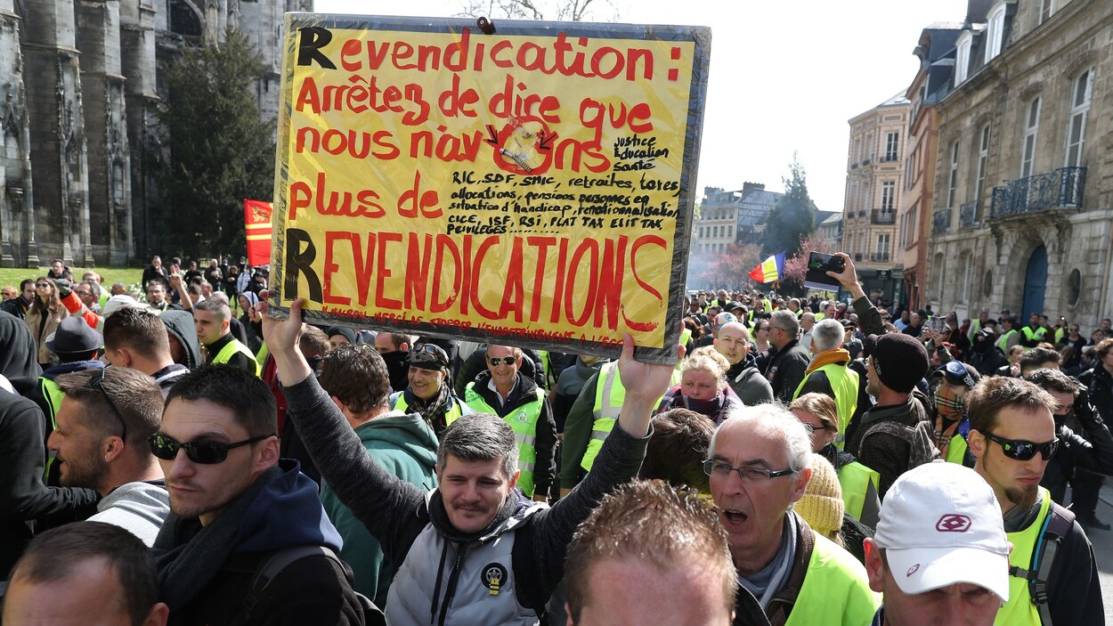 Une foule de manifestants, dont un tient une pancarte.