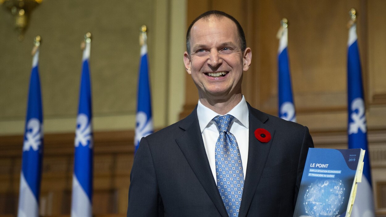 Eric Girard, souriant, tenant dans sa main gauche une copie de sa mise à jour économique.