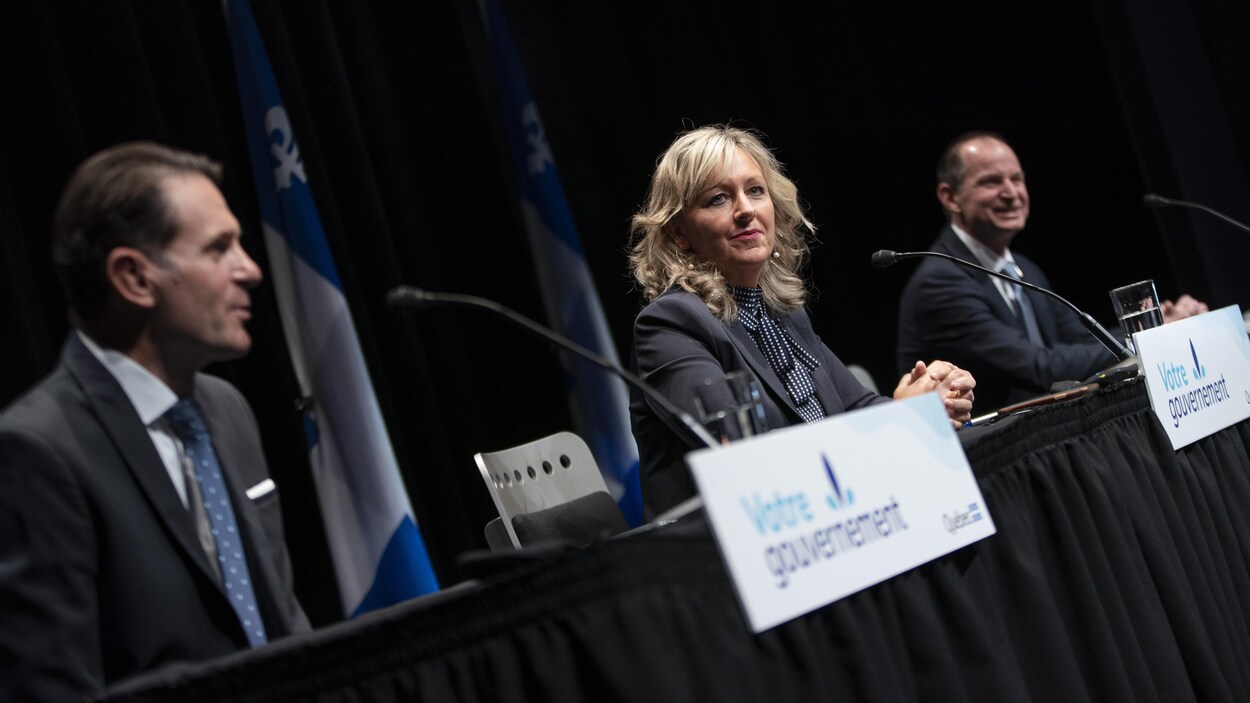 Trois personnes assises durant une conférence de presse.