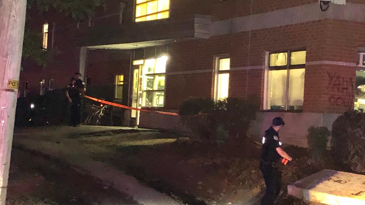 Deux policiers déploient un cordon de sécurité devant un immeuble de Gatineau, la nuit.