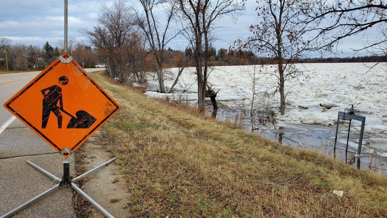 Un panneau d'avertissement orange à côté d'une route bordée de près par une rivière glacée.