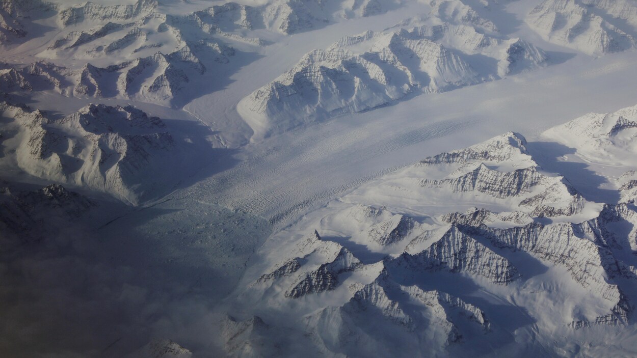 Des montagnes, toutes enneigées, sont photographiées des airs. Elles sont parfois séparées par une bande de glace. Des montagnes, toutes enneigées, sont photographiées des airs. Elles sont parfois séparées par une bande de glace.