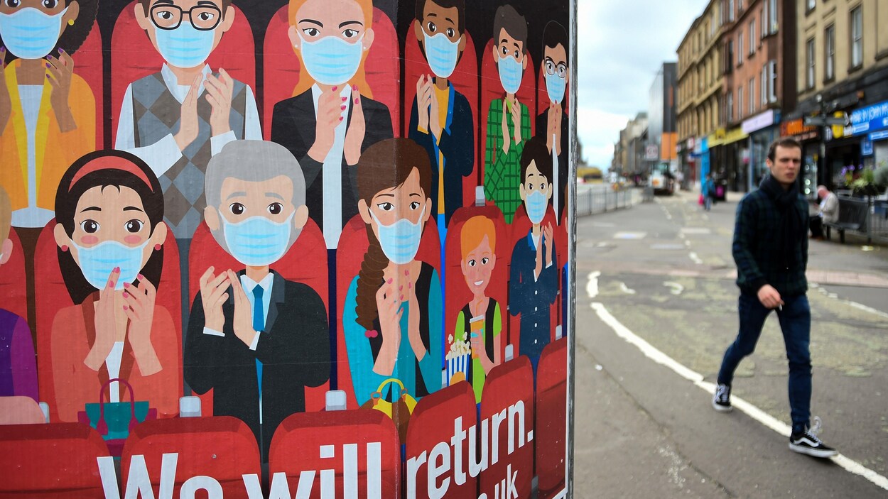Un homme marche dans la rue sans masque. Sur une affiche, on voit une dizaine de personnes portant le masque.