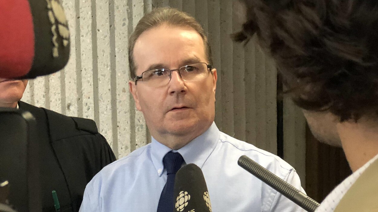 Glen Assoun répond aux questions des médias devant des micros et des caméras.