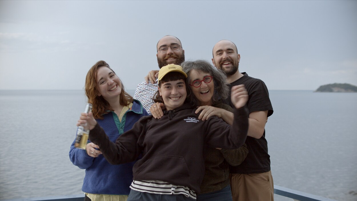 Une famille de cinq personnes devant un plan d'eau sourit à la caméra.