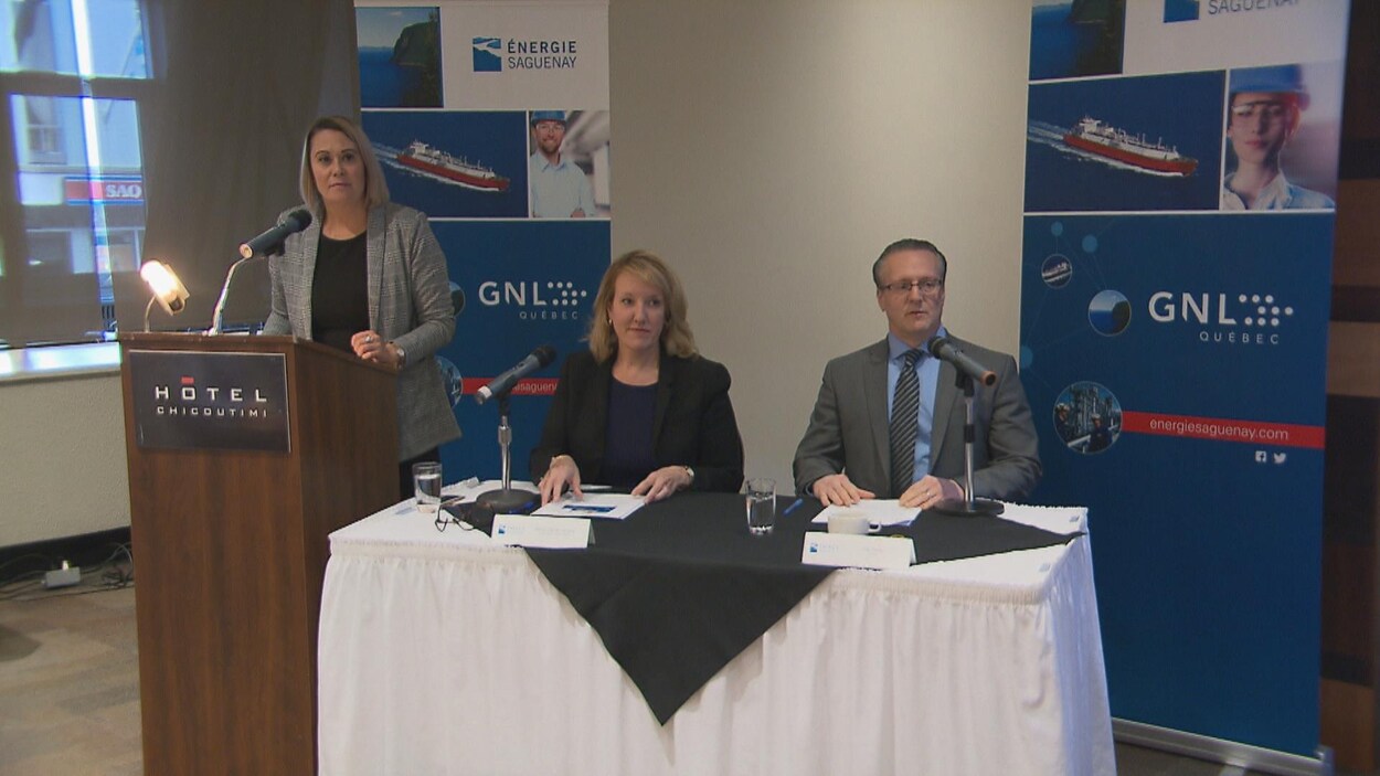 Un homme est une femme sont assis à une table. Il y a des affiches de GNL Québec derrière eux.