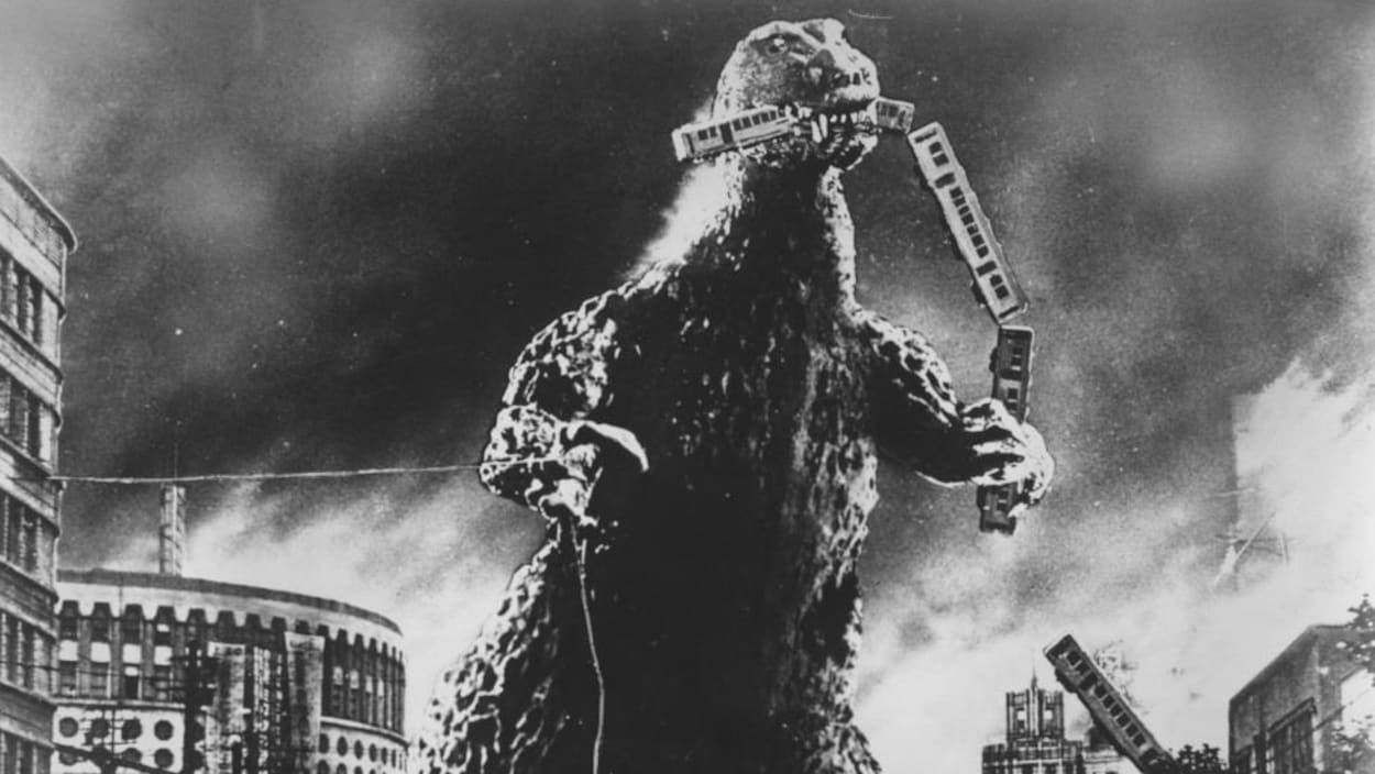 On voit le monstre « Gojira » en train de dévorer un train, dans une ville.