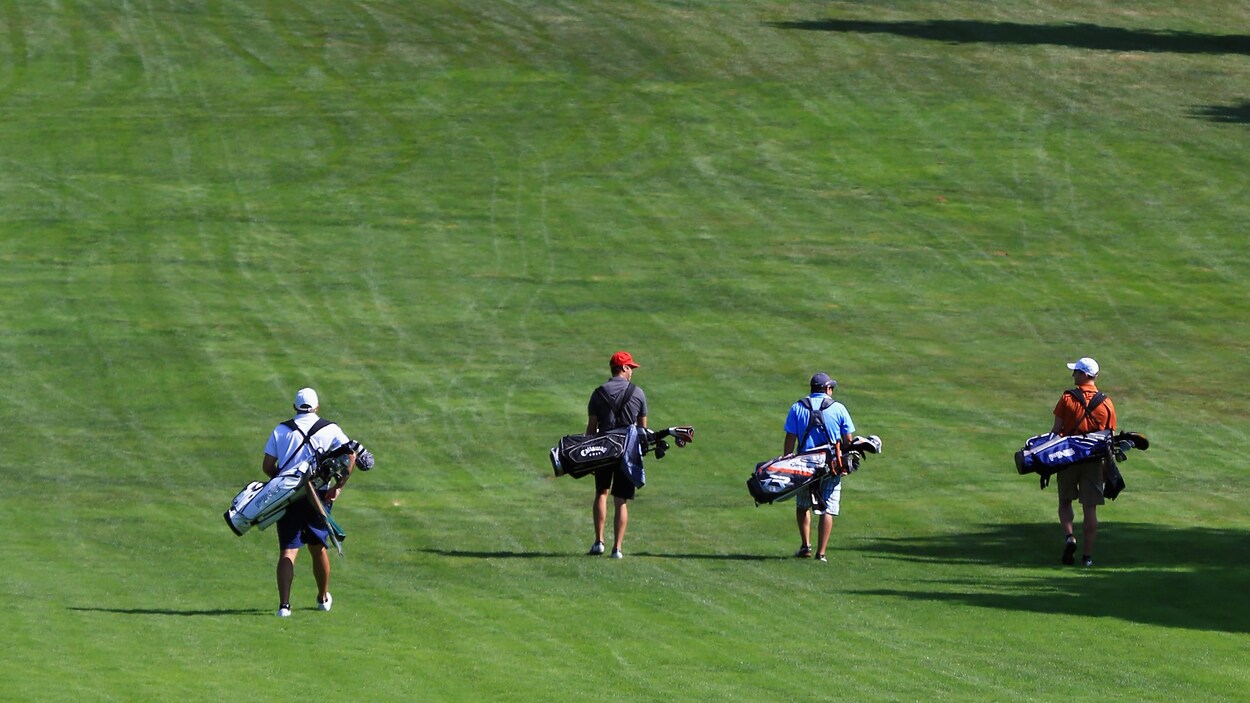 Quatre hommes marchent sur un terrain de golf avec leur sac en bandoulière.