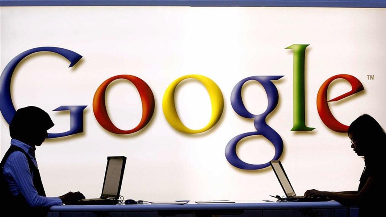 Deux personnes travaillent sur des ordinateurs devant le logo de Google.
