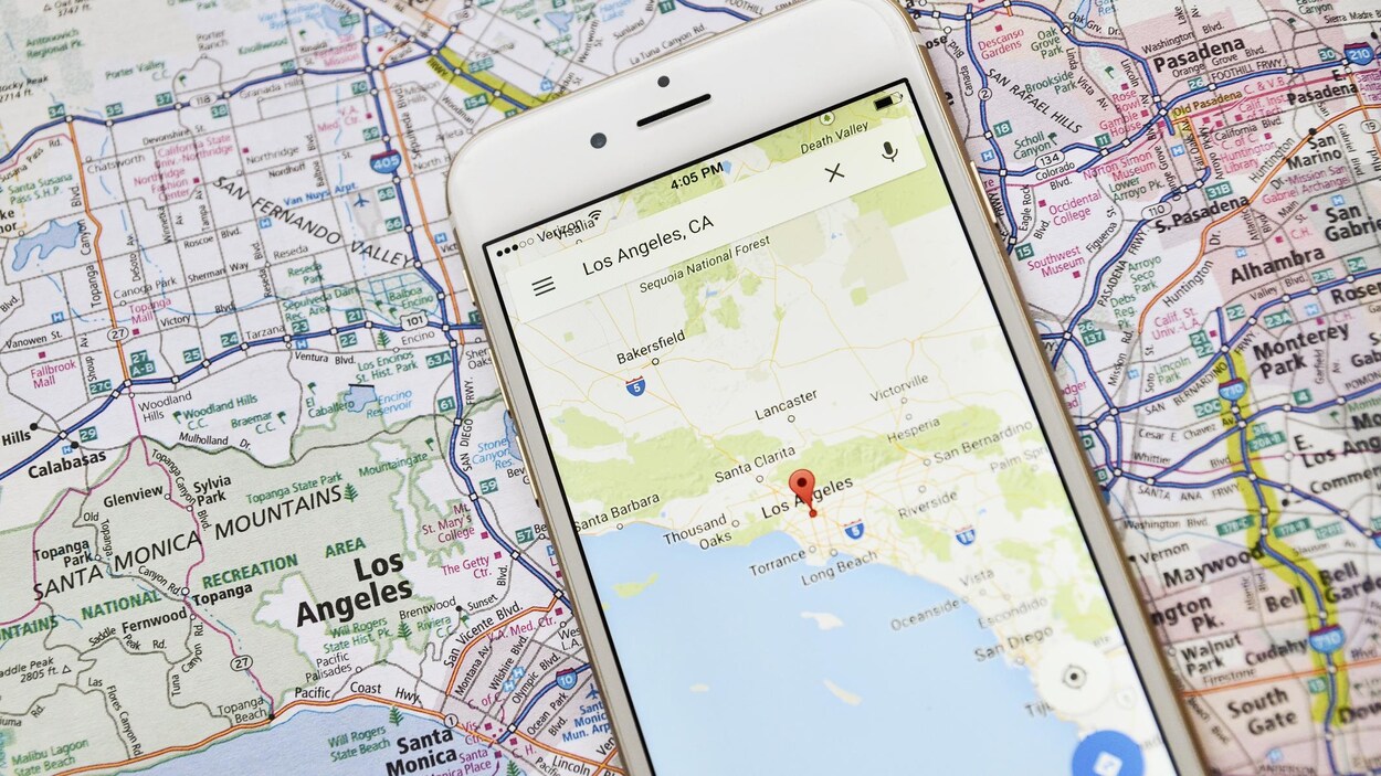 Une photo d'un téléphone déposé sur une carte géographique. L'écran du téléphone affiche une carte de la région de Los Angeles.