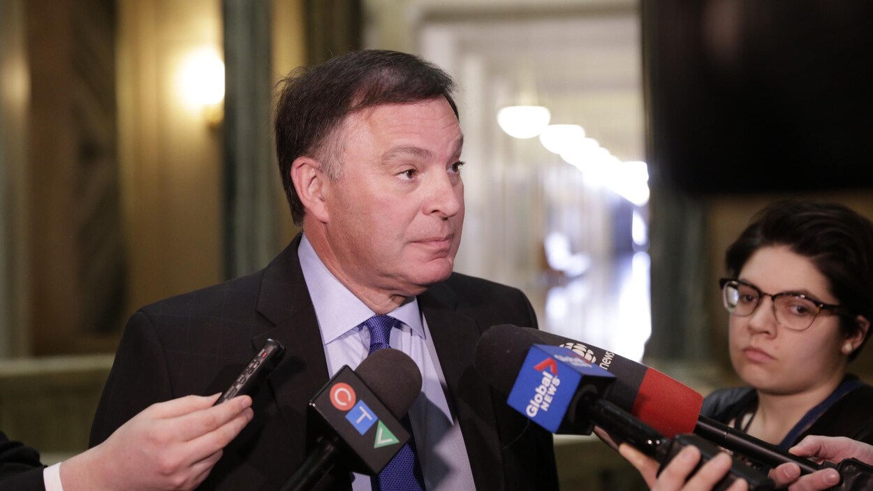 Le ministre de l'Éducation et vice-premier ministre Gordon Wyant devant des micros en train de répondre aux questions des journalistes.