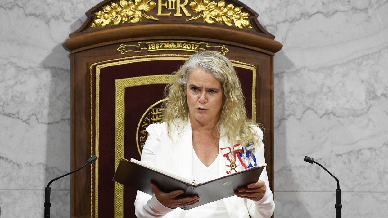 Julie Payette tient un cartable dans ses mains et parle assise dans un fauteuil.
