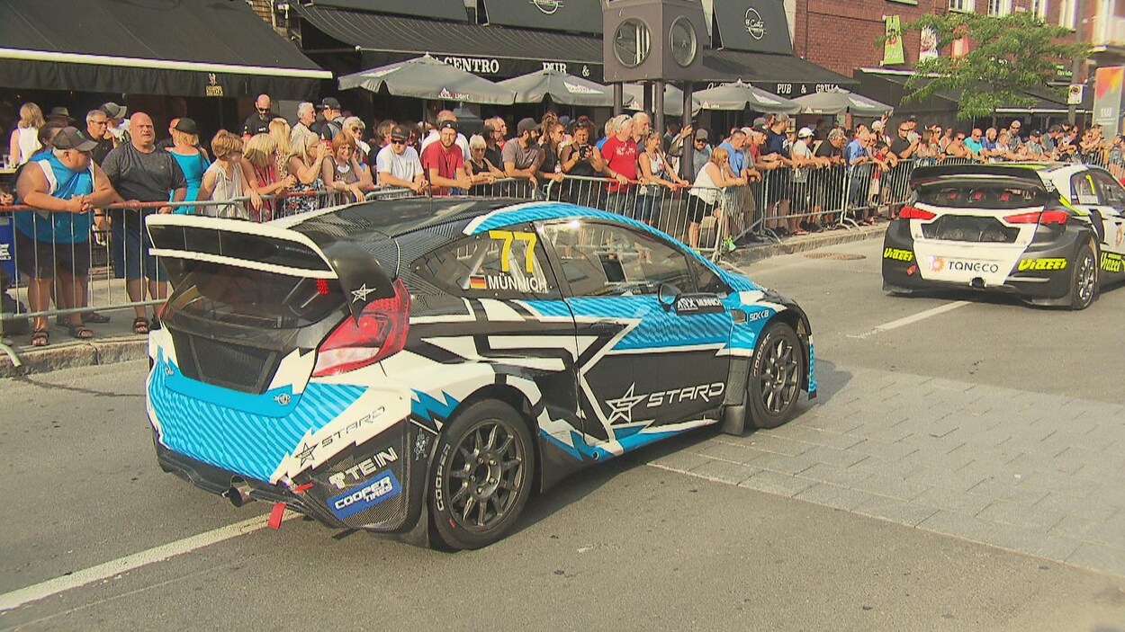 Derrière un barrière, des gens regardent des voitures de course défiler.