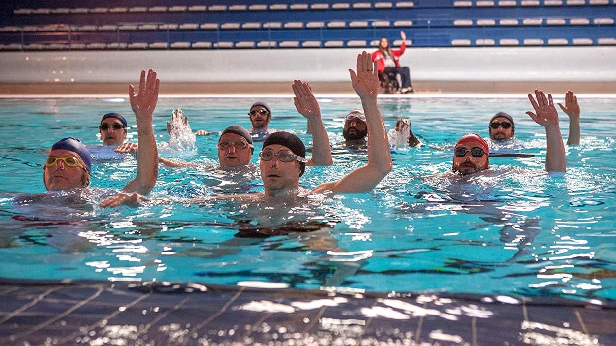 Des hommes sont dans une piscine et lèvent la main.