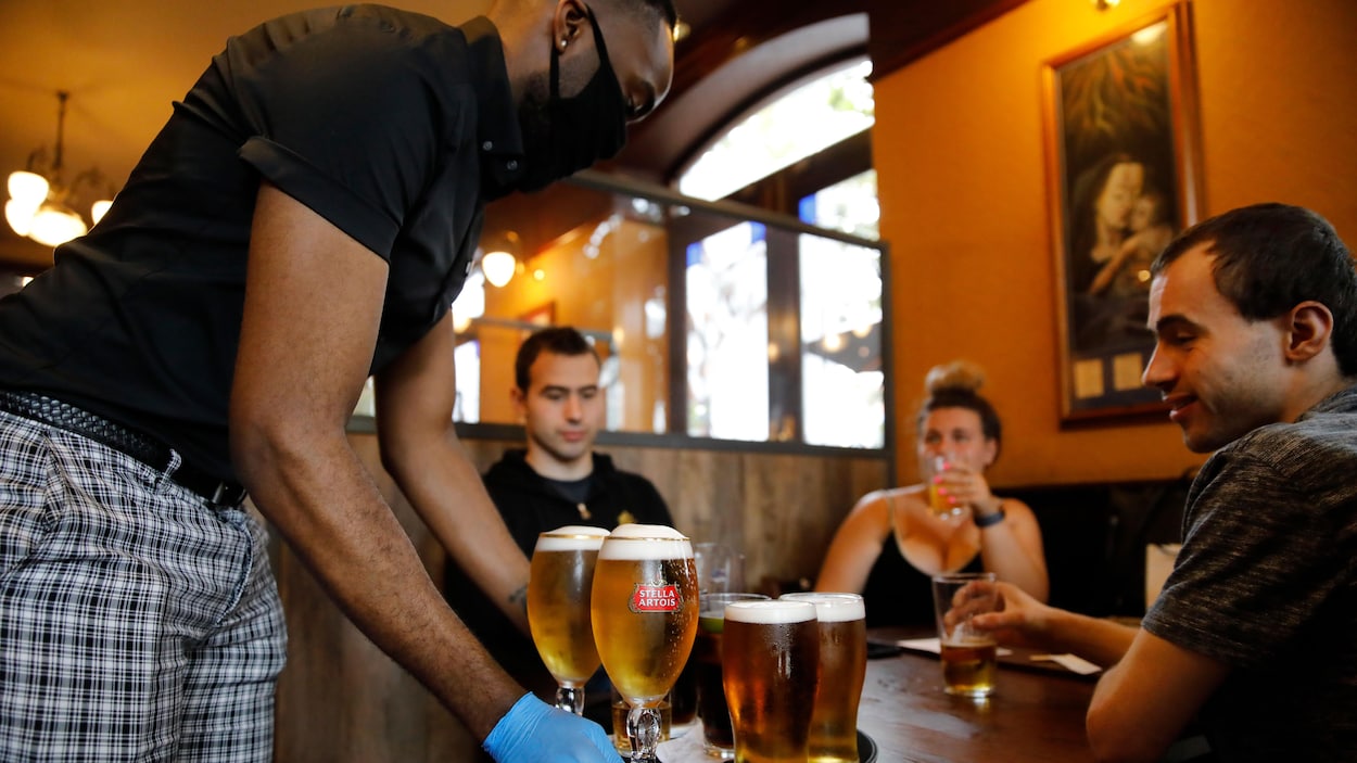 Un homme portant un masque de protection et des gants sert de la bière à des clients.