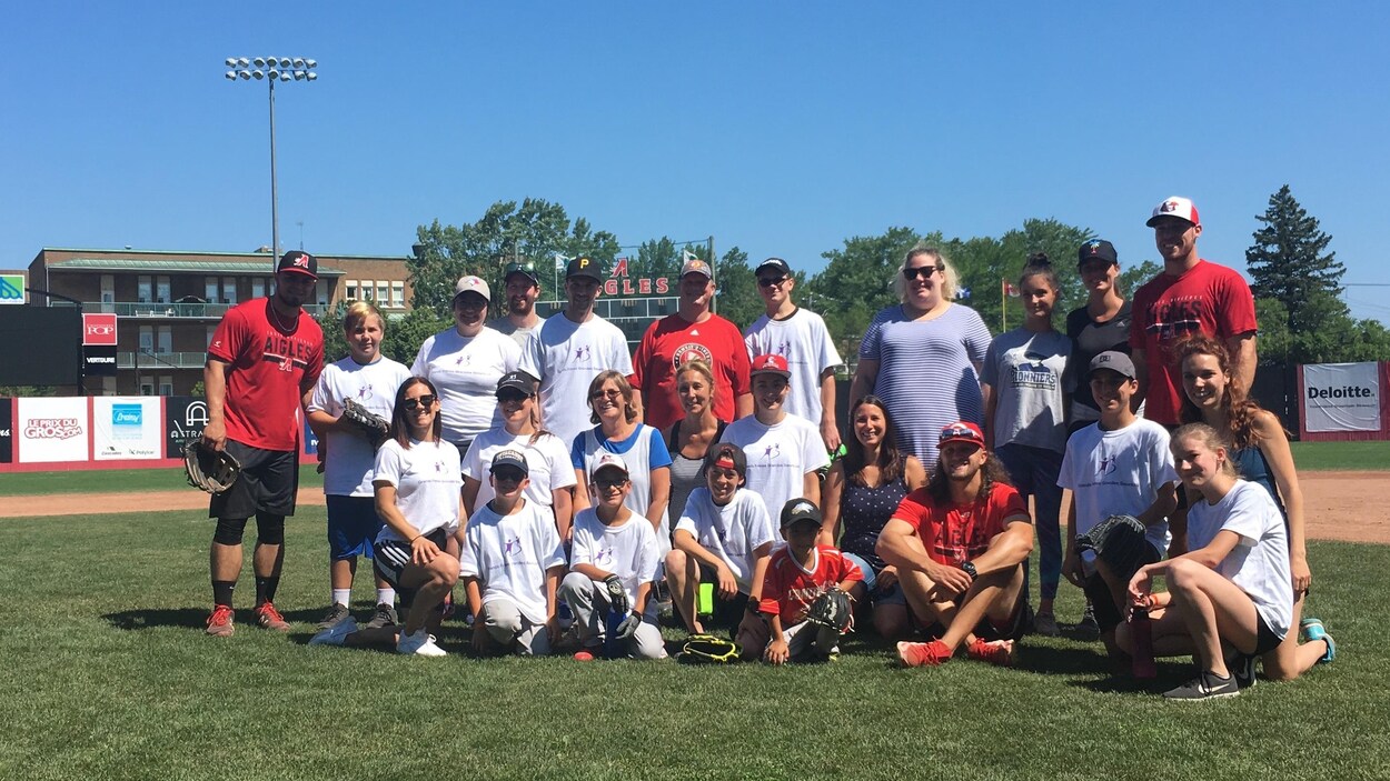 Une vingtaine de personnes posent ensemble devant un terrain de baseball.