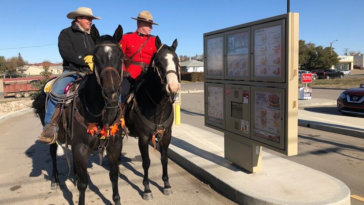 Deux hommes, chacun sur un cheval, en train de commander au service au volant d'un Tim Hortons en Saskatchewan.