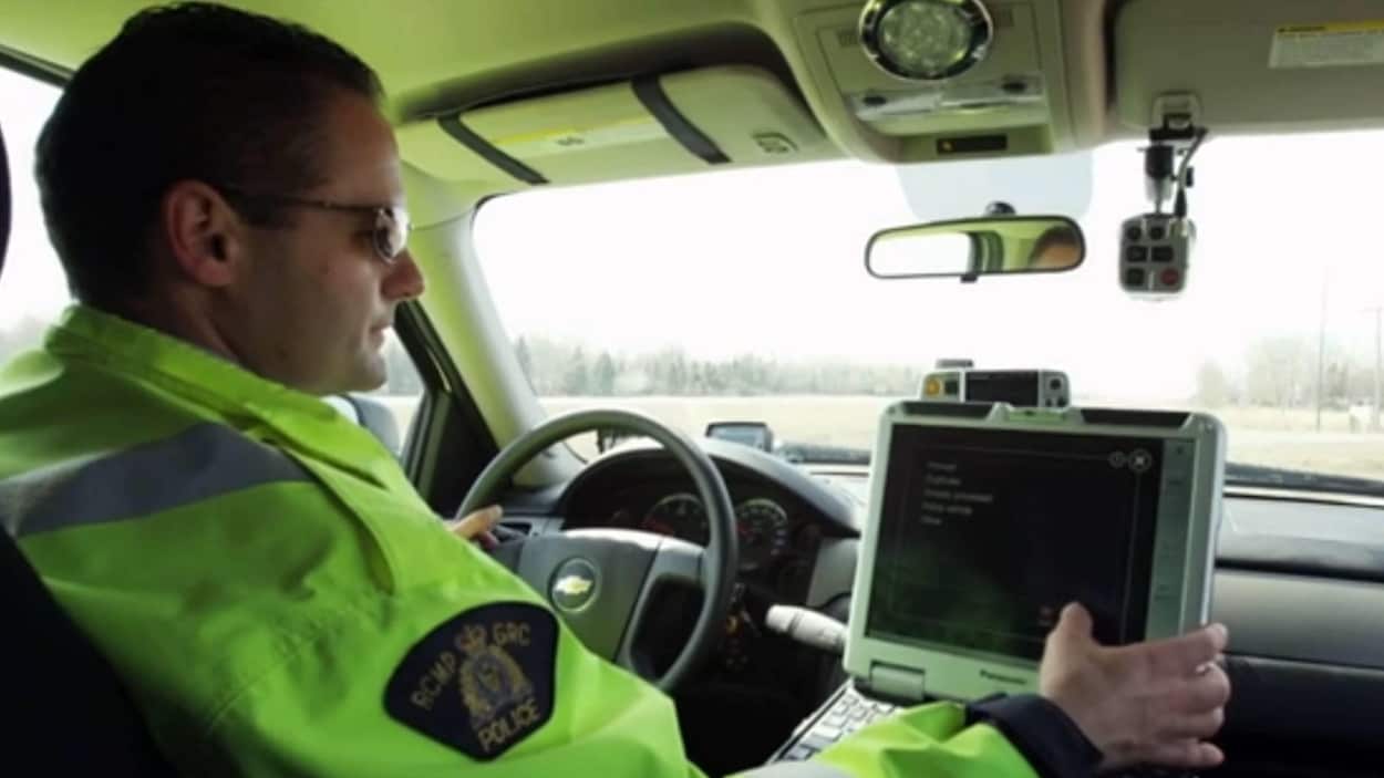 Un agent de la GRC porte un gilet de couleur fluorescente. Il est au volant d'une voiture.
