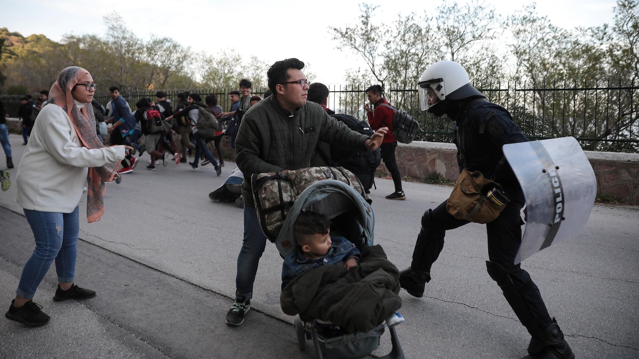 Un policier frappe un homme tenant une poussette.