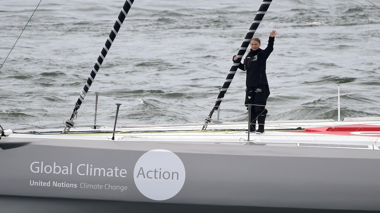 La jeune militante suédoise du climat Greta Thunberg, sur le voilier, salue les médias en levant la main droite.