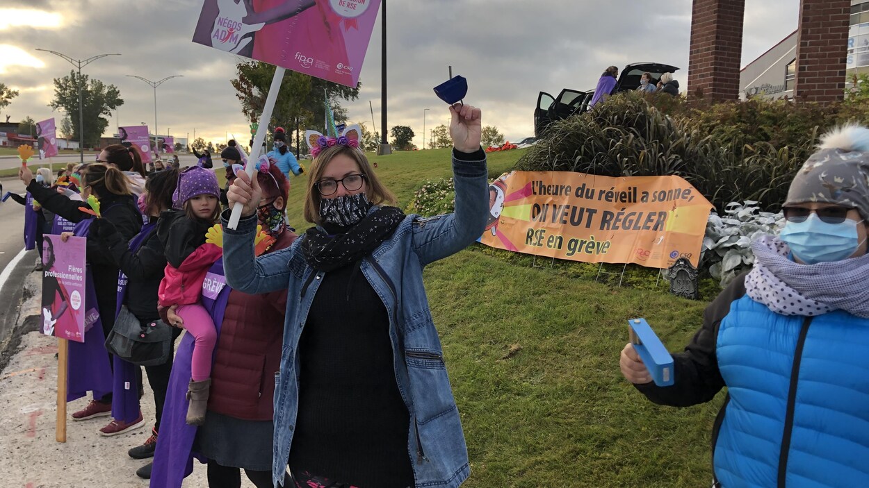 Des éducatrices avec des pancartes et des clochettes manifestent en bordure du boulevard de l'Université.